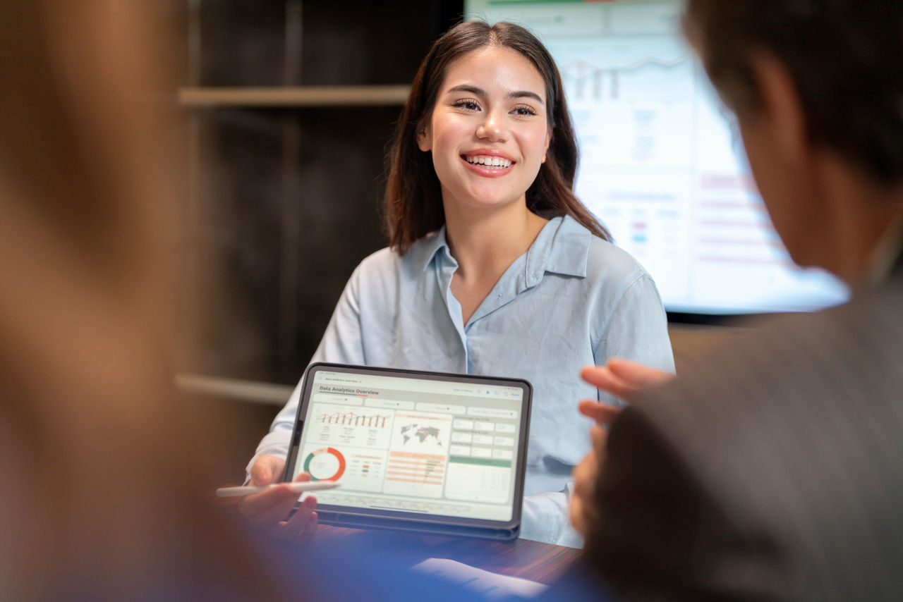 An employee holding a computer with two others looking on at the display on her screen.