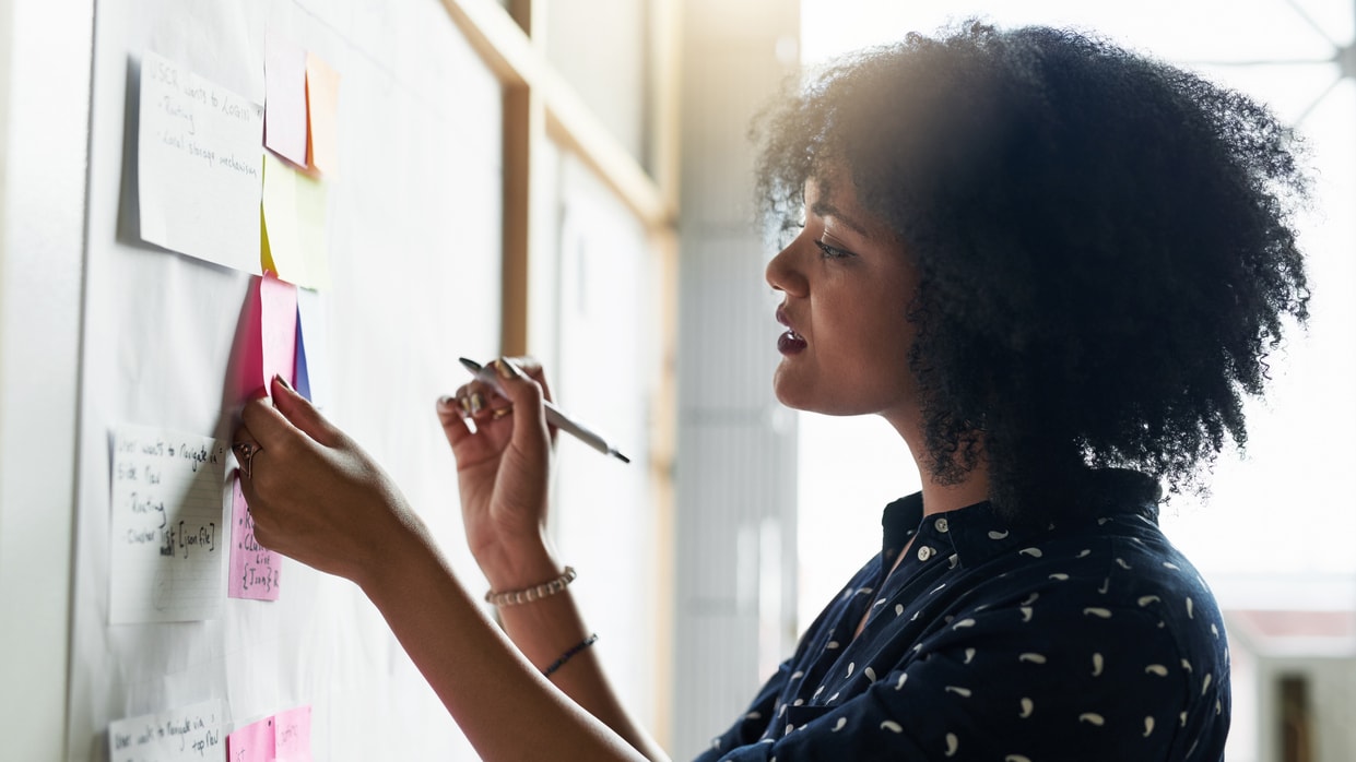A woman writing on a whiteboard with sticky notes.