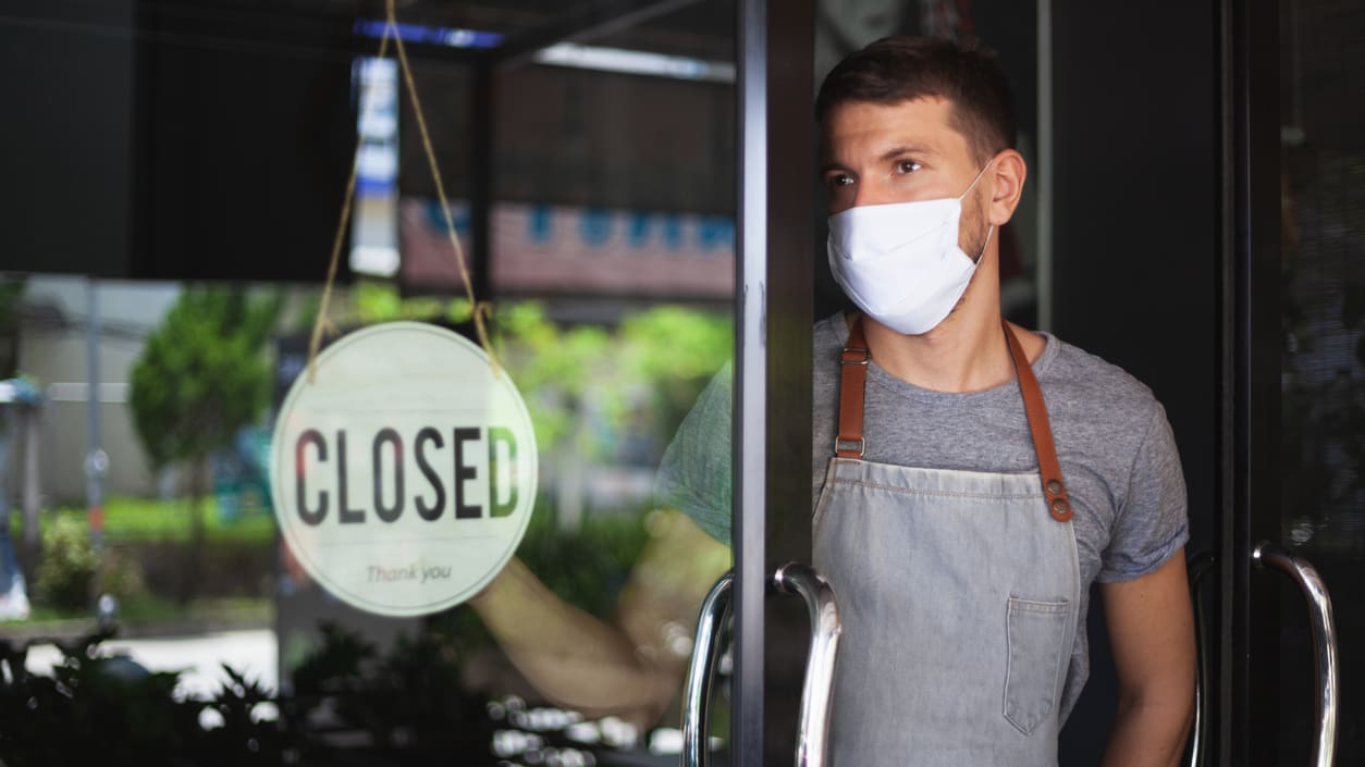 A man wearing a face mask in front of a closed sign.