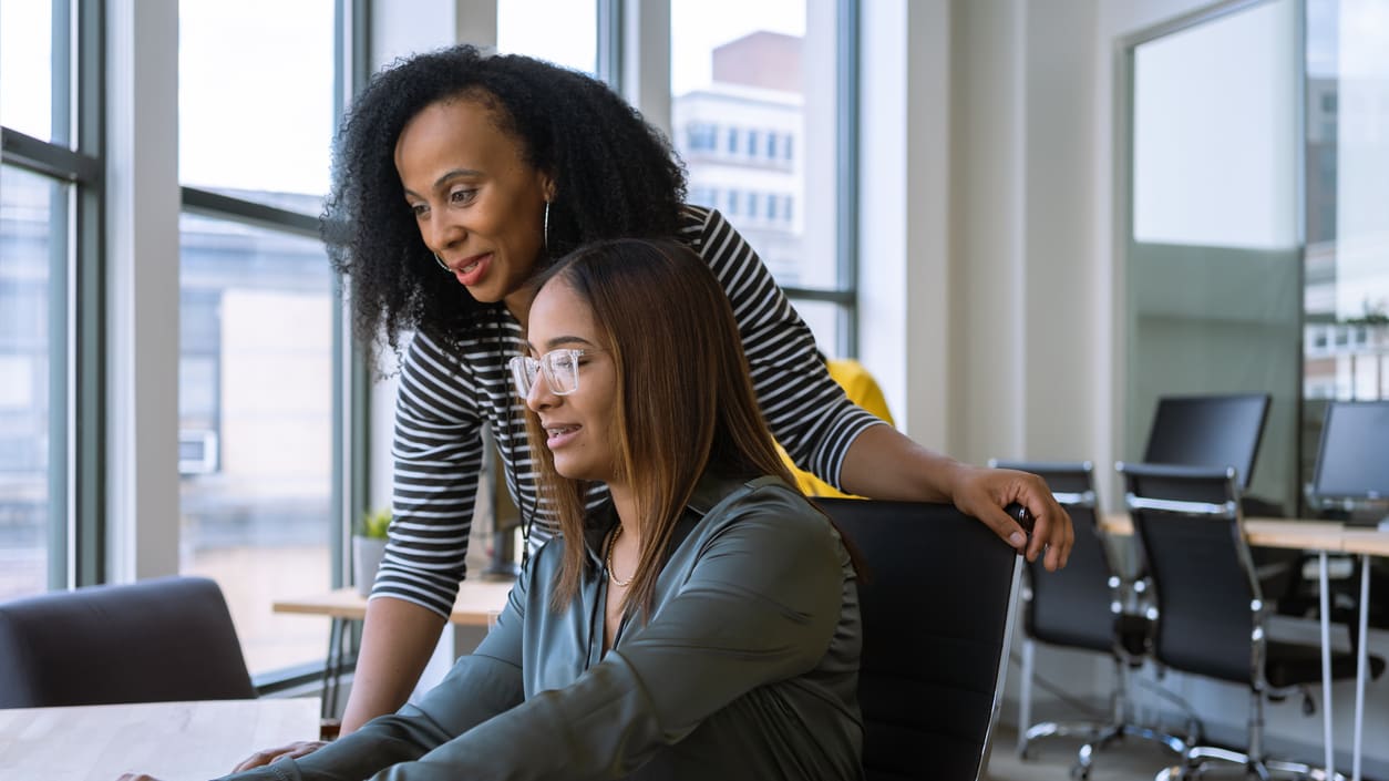 Two women working on a laptop in an office.