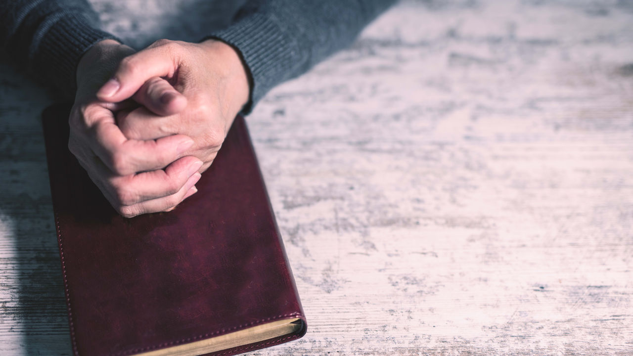 A person holding a bible on a wooden table.