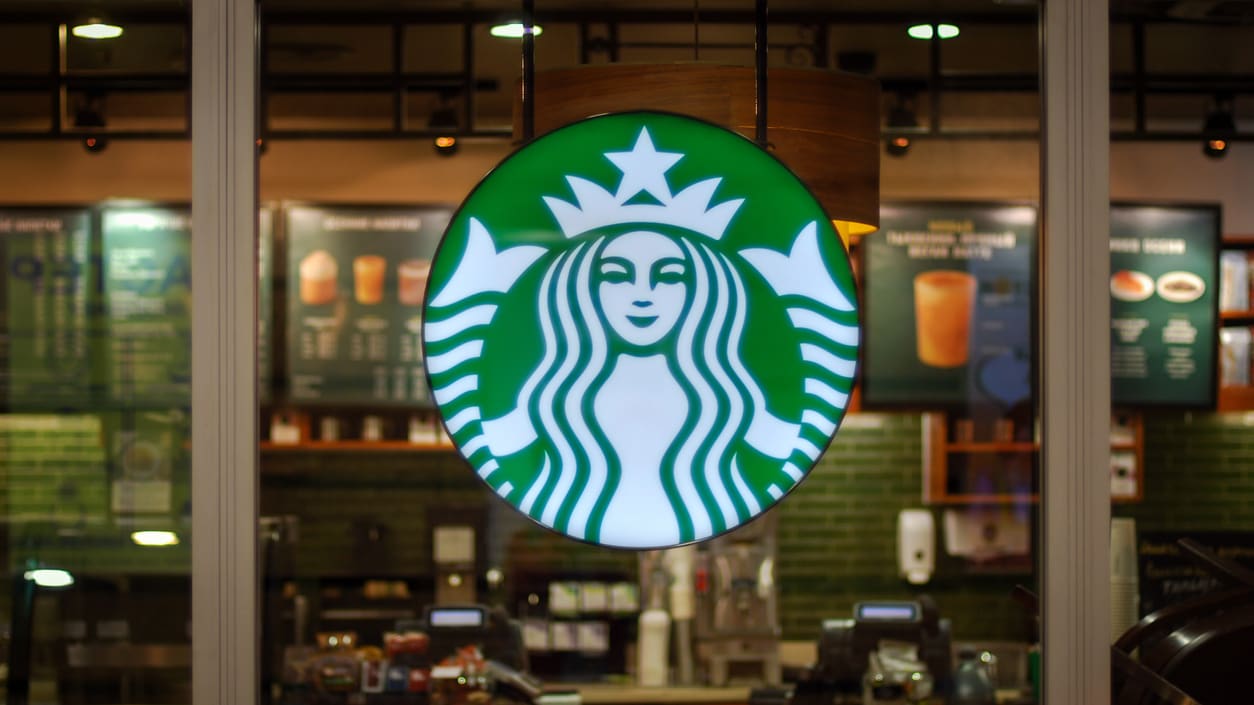 A starbucks sign is seen through a glass door.