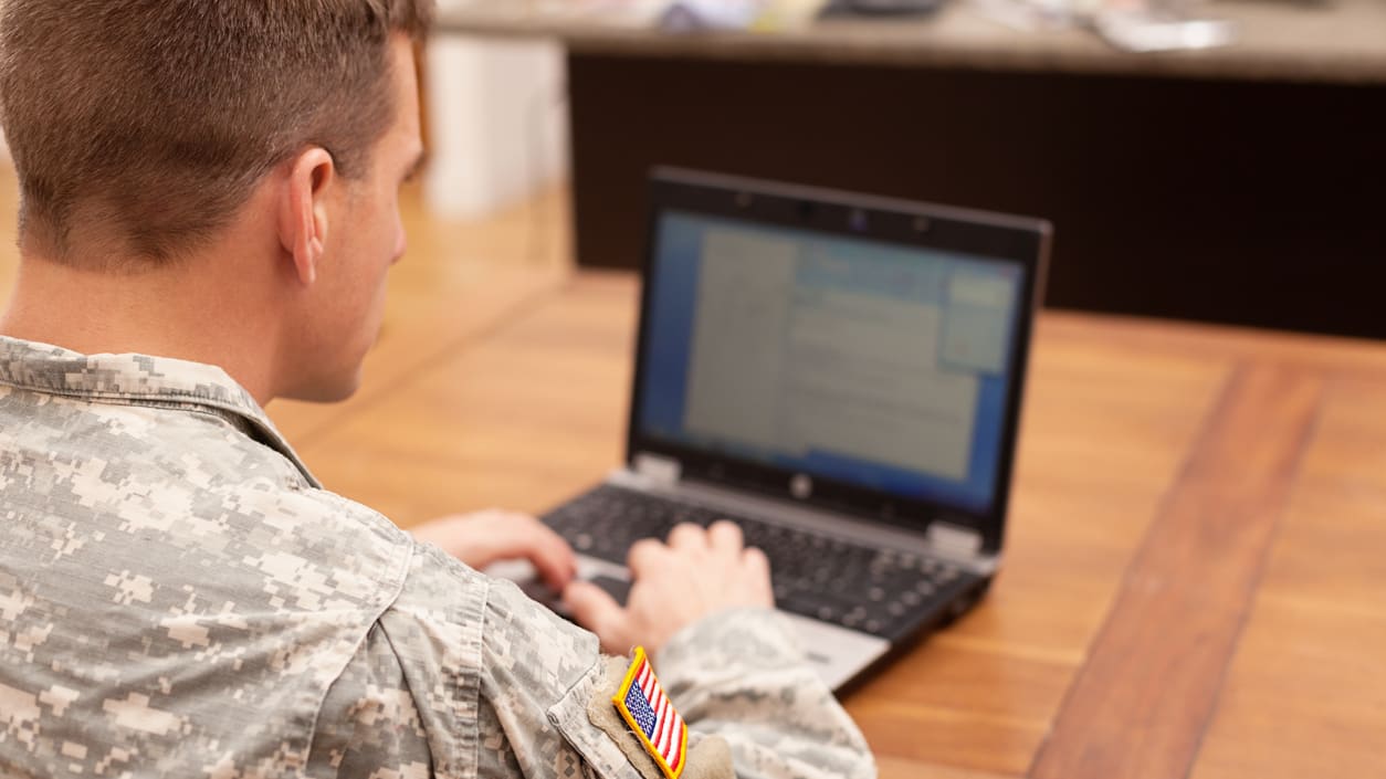 A soldier is using a laptop on a table.