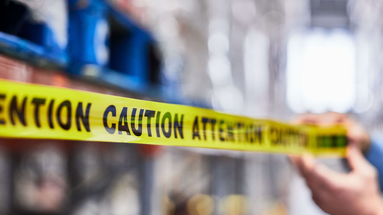 A person is holding a yellow caution tape in a warehouse.