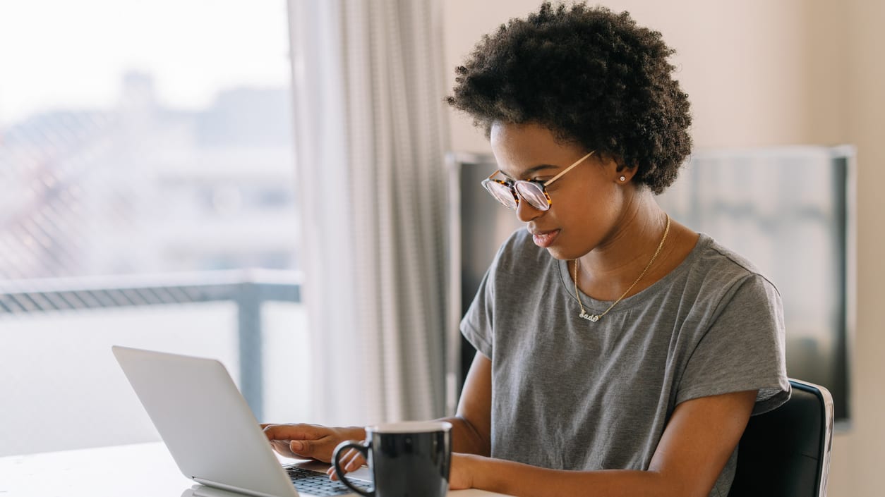 A woman working on a laptop in front of a window.