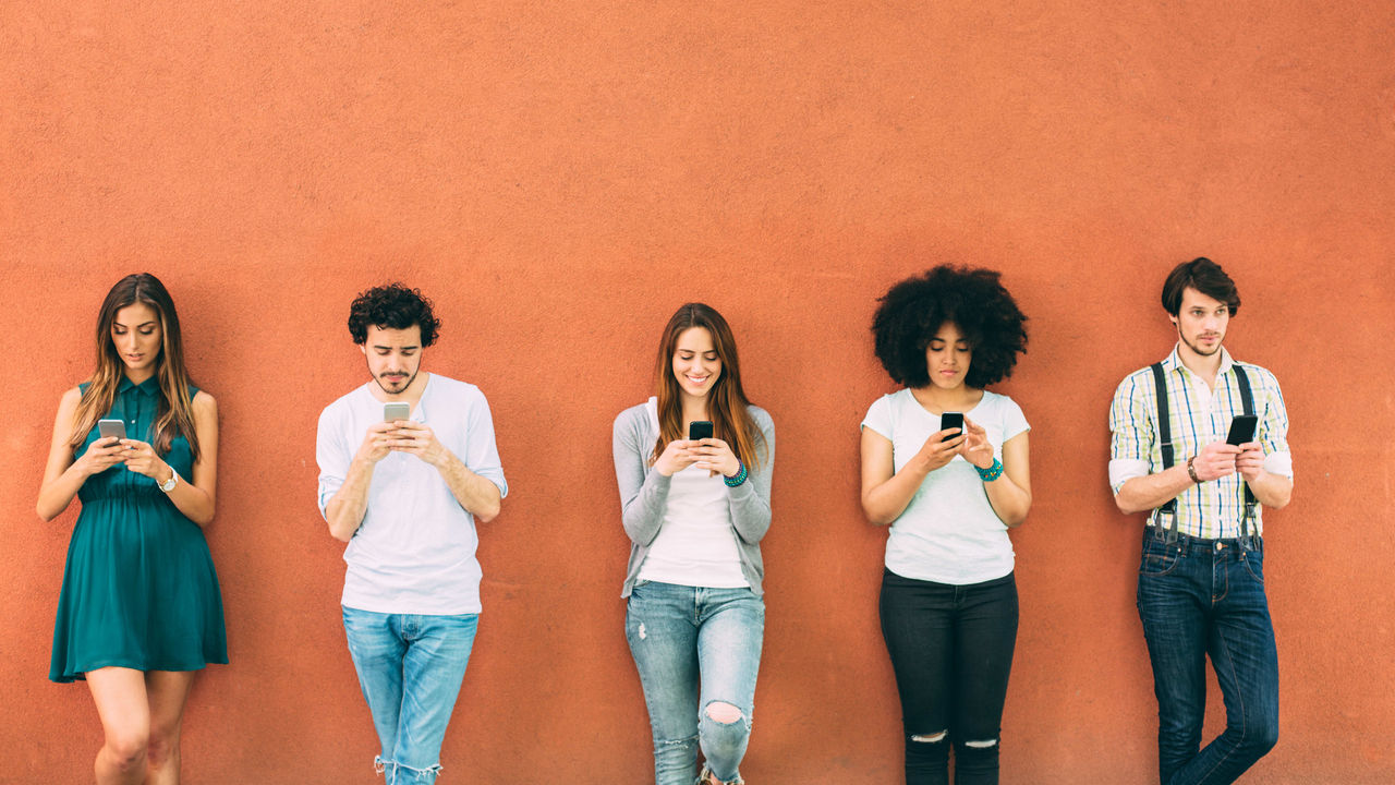 A group of people standing in a line looking at their phones.