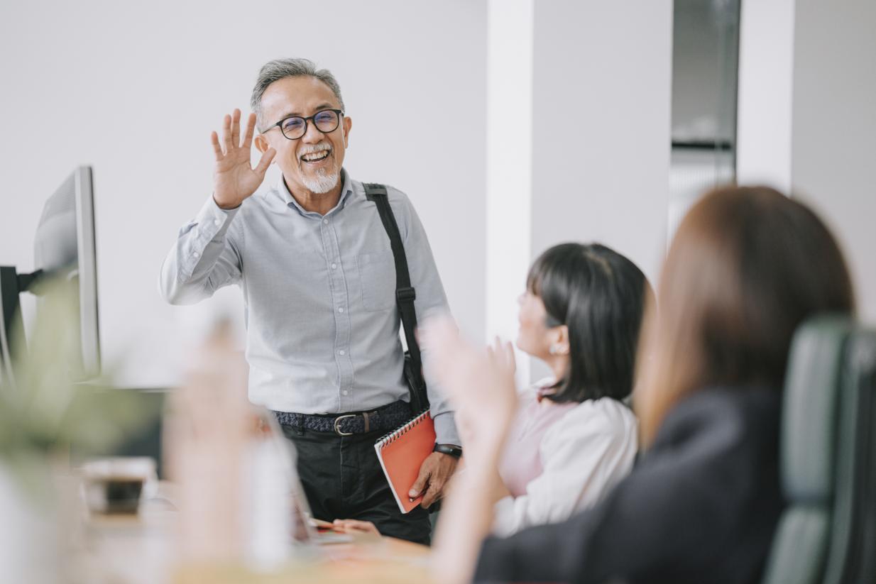 man with gray hair and beard waves at colleagues