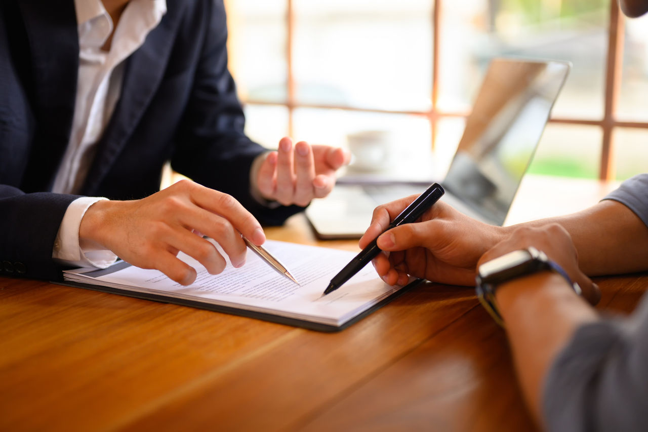 Closeup of one person's hands pointing at contract showing client where to sign.