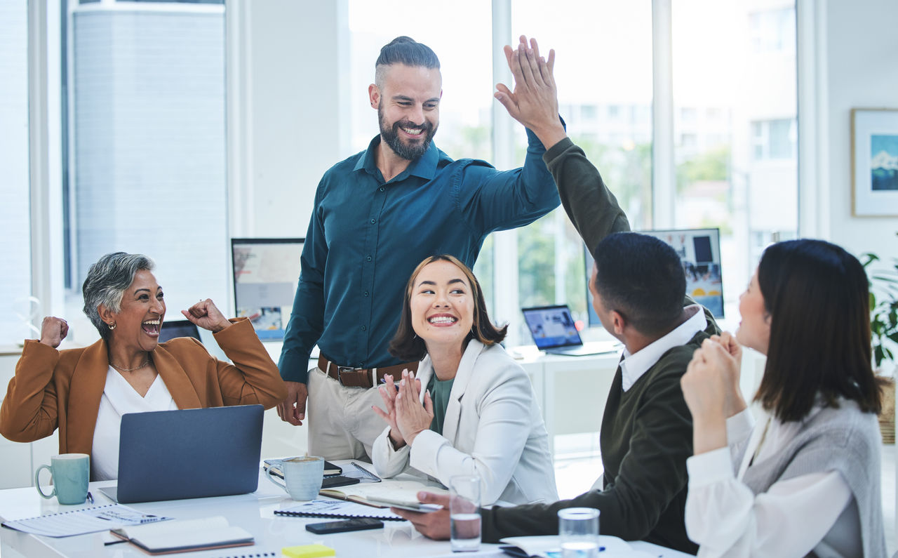 Employees celebrate a work success in an office with high fives and smiles