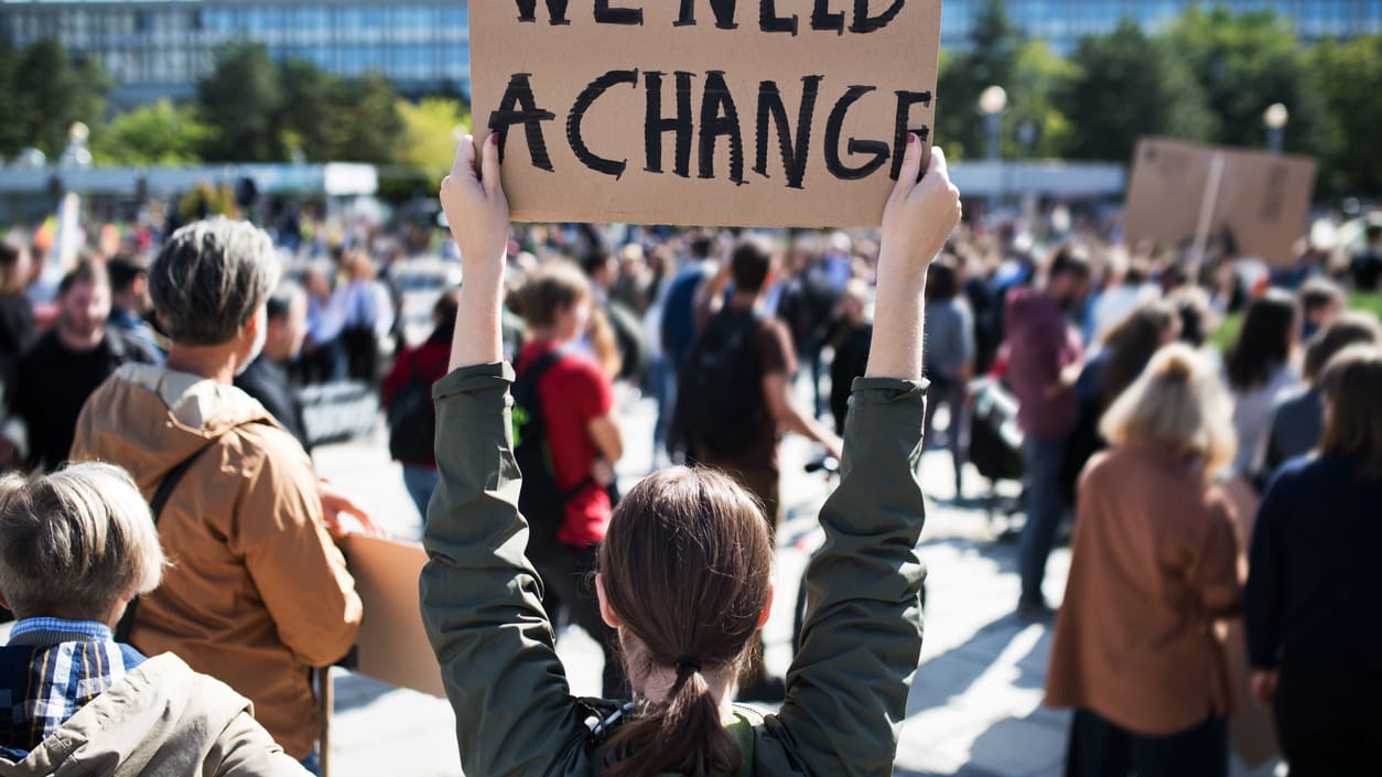 A woman holding up a sign that says we need a change.