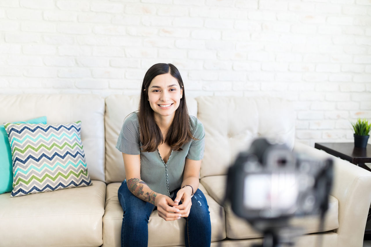 1157629162 Smiling vlogger streaming live through camera at home