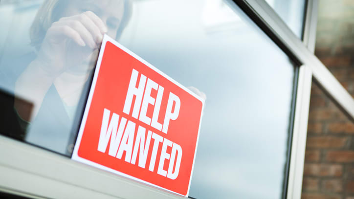 A woman holding up a sign that says help wanted.