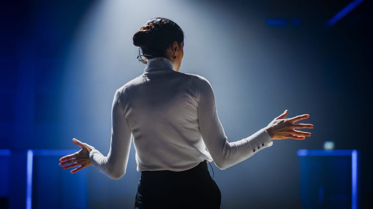 A woman is standing on stage with her arms outstretched.